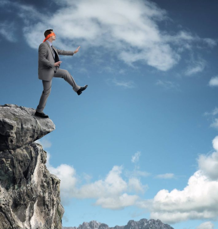 Businessman in a blindfold stepping off a cliff ledge concept for risk, challenge, conquering adversity or ignorance